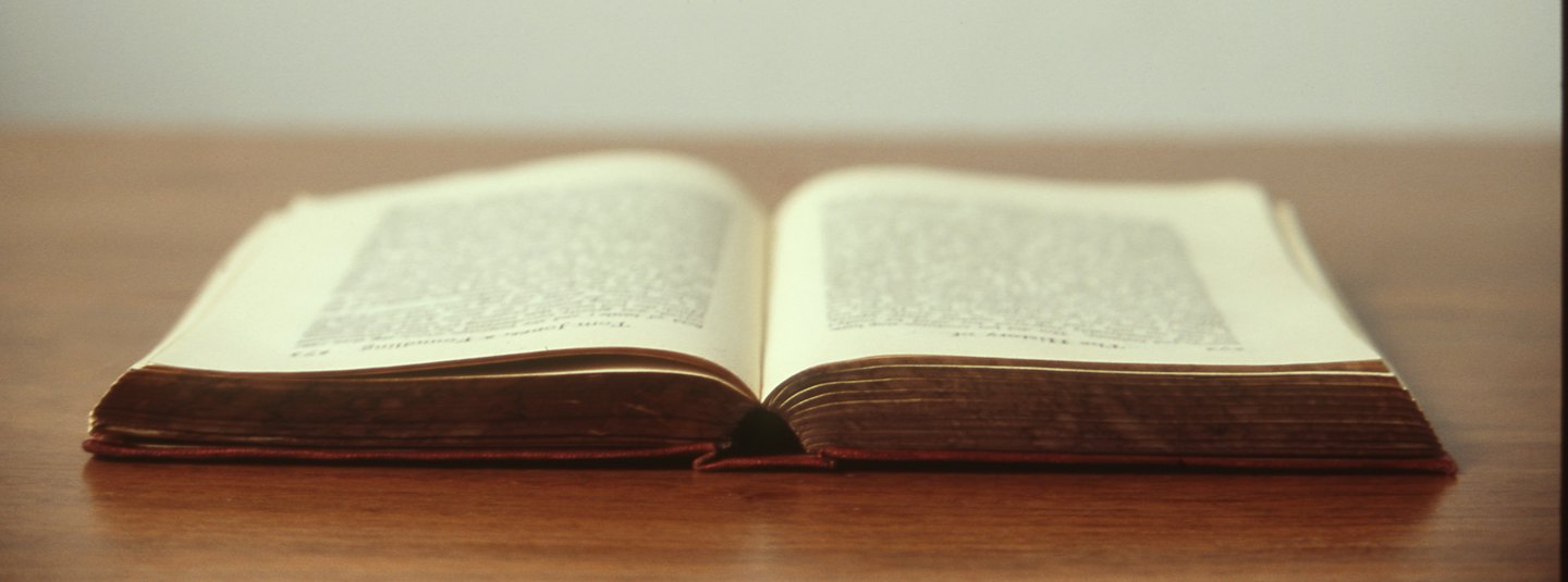 Ein aufgeschlagenes, altes Buch liegt auf einem polierten Holztisch.